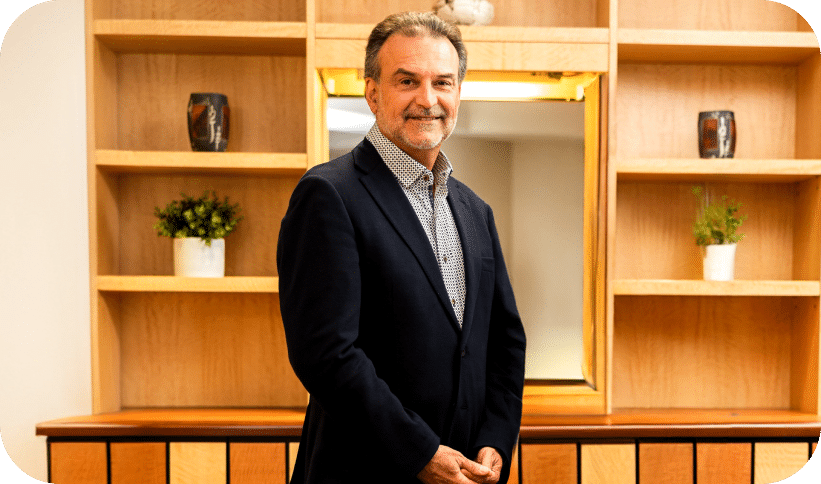 A man in a suit stands confidently in front of a wooden shelf filled with various items.