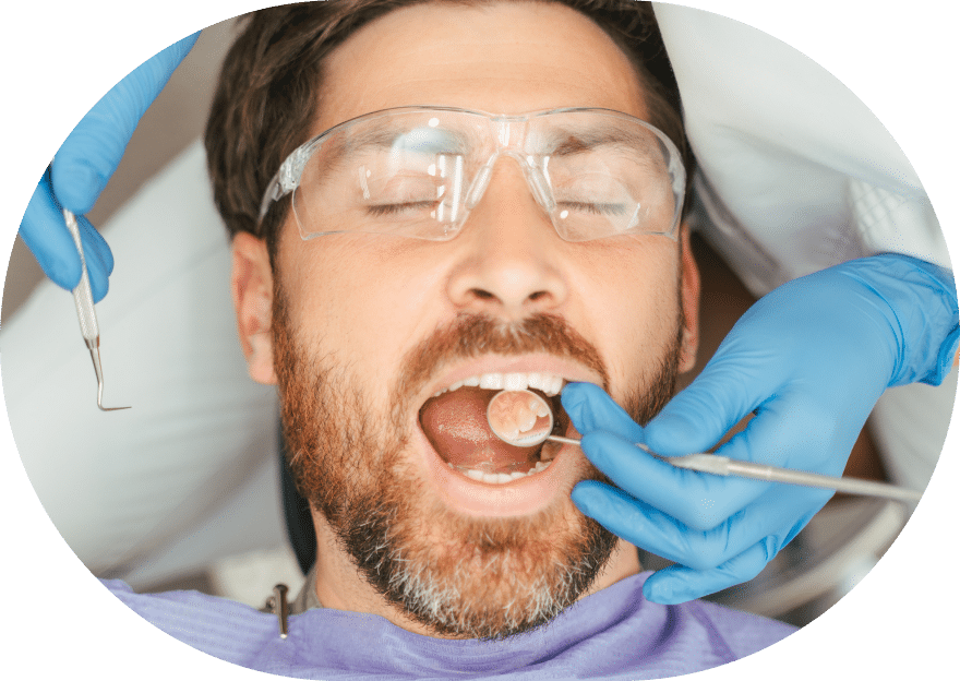 A man receiving a dental cleaning, seated in a dentist's chair with dental tools and equipment visible.