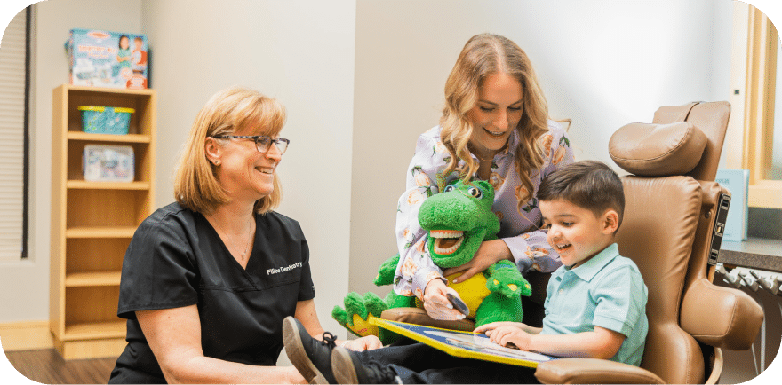 A woman and two children are seated in a chair, with a stuffed frog resting in the children's laps.