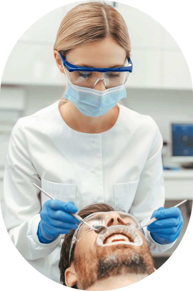 A woman in a dental office attends to a patient seated in a dental chair, surrounded by dental equipment and tools.