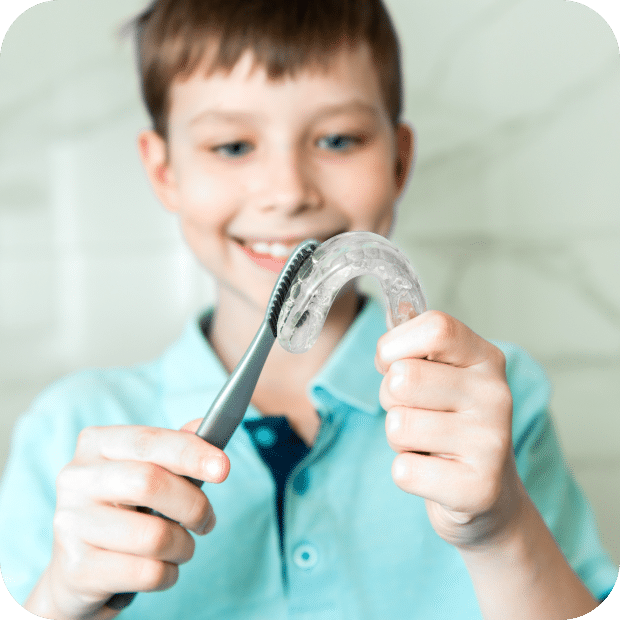 A young boy smiles while holding a toothbrush and a tube of toothpaste, ready for his dental care routine.