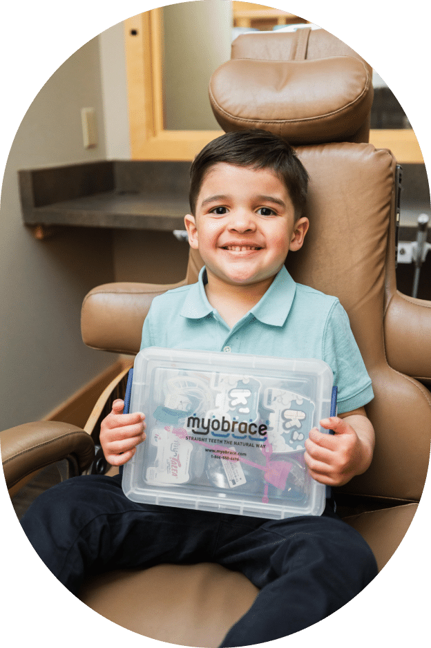 A young boy seated in a chair, holding a box with a focused expression on his face.