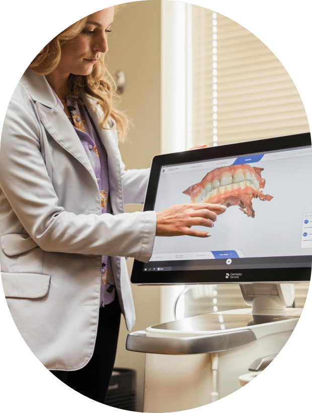 A woman in a dental office demonstrates a patient's mouth using a computer, highlighting dental care technology