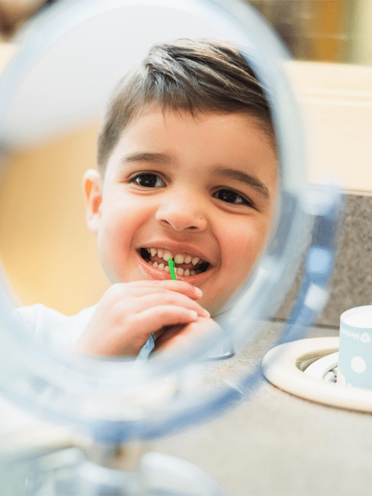 A young boy brushes his teeth in front of a mirror, focusing on his dental hygiene routine