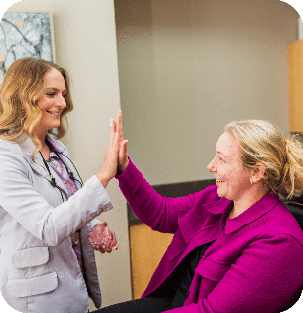 A woman enthusiastically high-fives a doctor, celebrating a positive moment in a healthcare setting