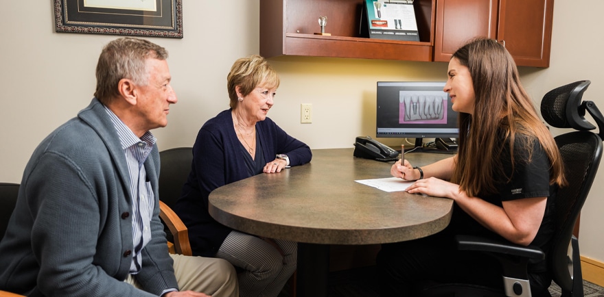 A woman and man consult with a doctor at a desk, engaged in a discussion about health matters