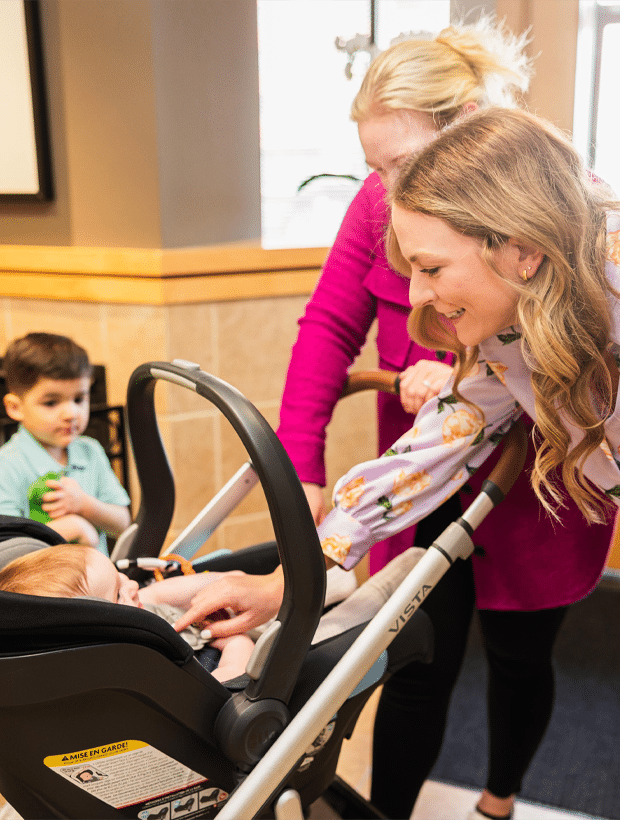 A woman confidently pushes a baby in a stroller along a sunny path, enjoying a pleasant day outdoors