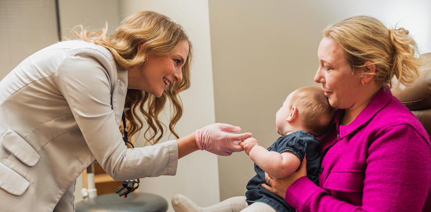 A woman holds a baby as a doctor conducts an examination, showcasing a moment of care and medical attention