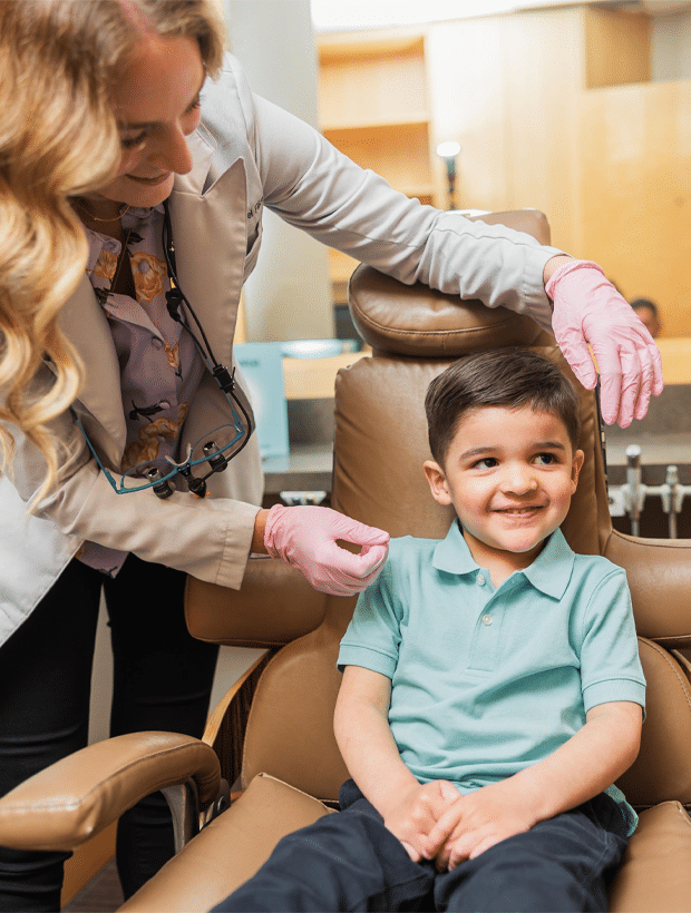 A woman sits in a chair, smiling at a young boy who is playfully engaged beside her