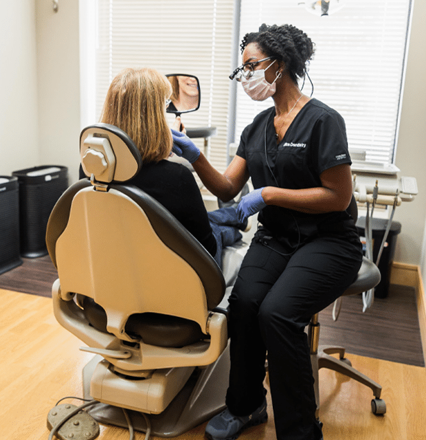 A woman seated in a dental chair, wearing a mask, appears calm during her dental appointment