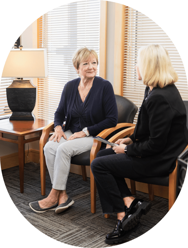 A woman seated in a chair engages in conversation with another woman nearby.