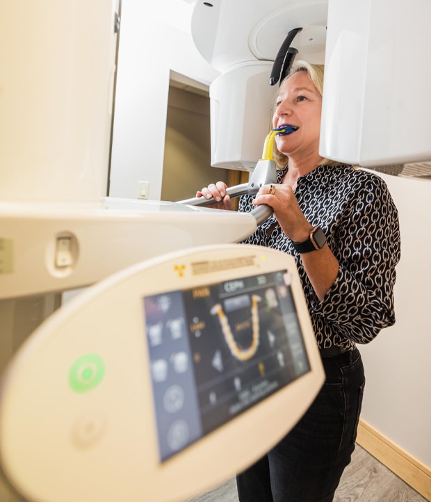 A woman is using a dental device while seated in a dental office, surrounded by dental equipment and tools