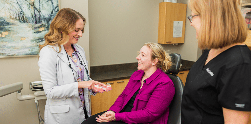 A woman converses with another woman seated in a dental chair, showcasing a supportive dental environment