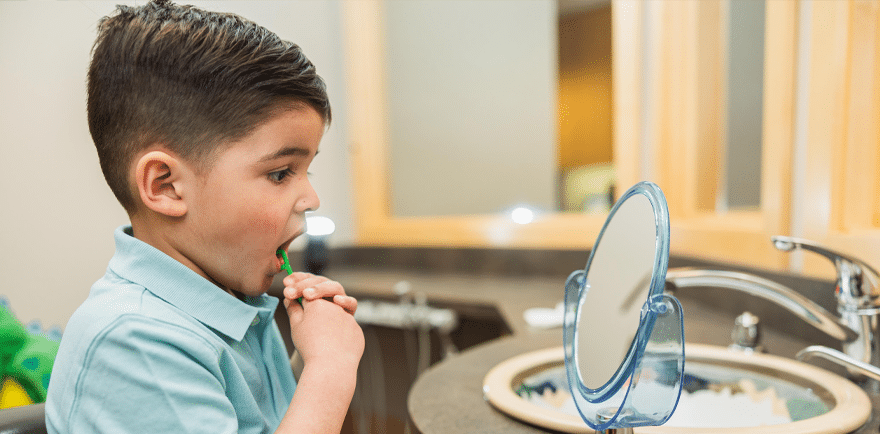 A young boy brushes his teeth in front of a mirror, focusing on his dental hygiene routine