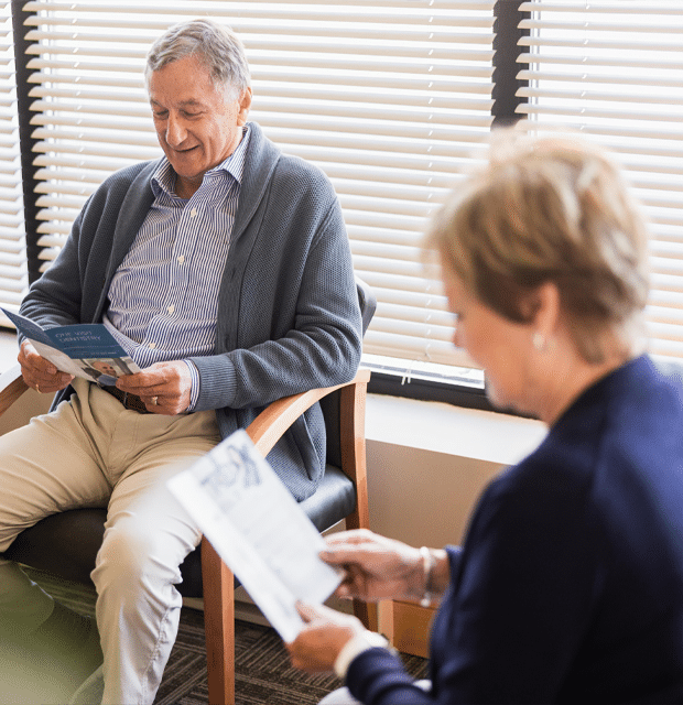 A man seated in a chair, engrossed in reading a magazine, with a relaxed expression on his face