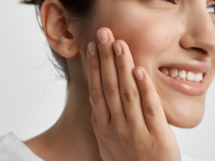 A woman smiles warmly while gently resting her hand against her face