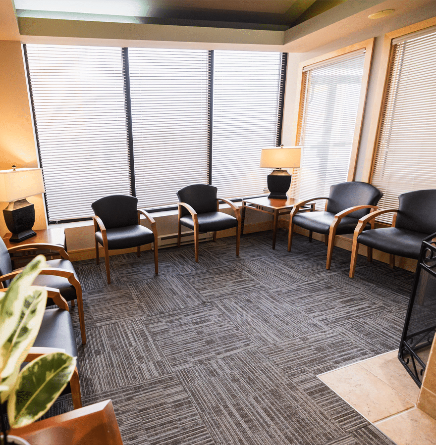 A cozy waiting room featuring comfortable chairs arranged around a warm fireplace