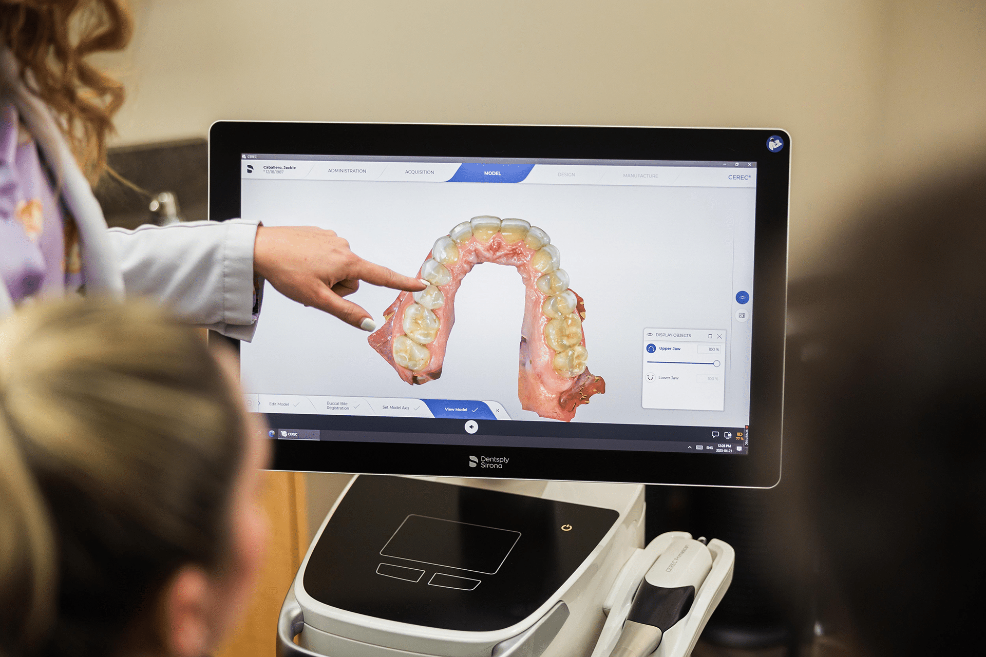 A woman demonstrates a patient's dental condition using a computer, highlighting the teeth on the screen