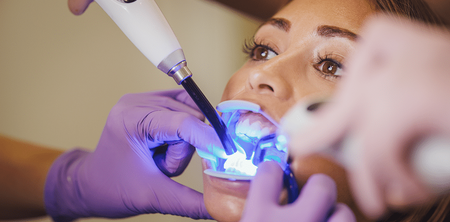 A woman undergoing a dental cleaning procedure with a dental instrument in a clinical setting